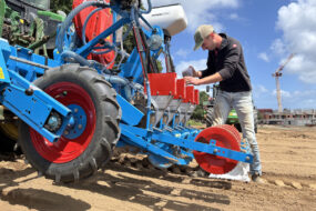 Un homme entrain de remplir un semoir attelé à un tracteur dans un champ