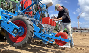Un homme entrain de remplir un semoir attelé à un tracteur dans un champ