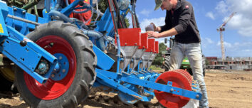 Un homme entrain de remplir un semoir attelé à un tracteur dans un champ