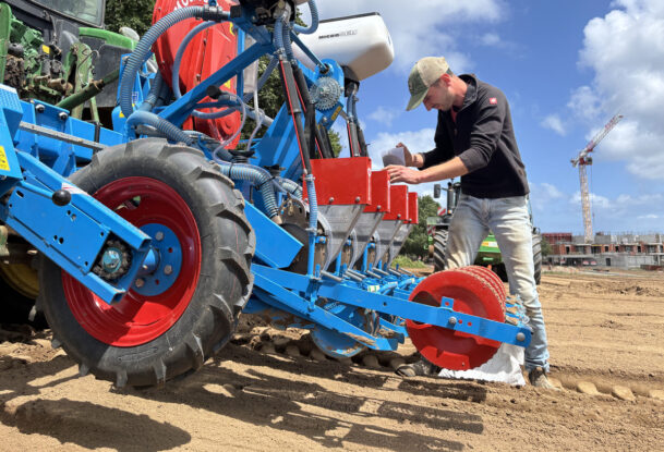 Un homme entrain de remplir un semoir attelé à un tracteur dans un champ