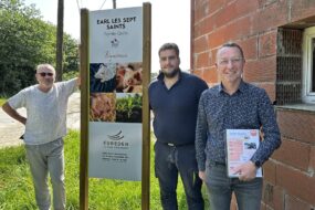 Trois hommes posent devant une pancarte