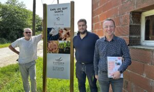 Trois hommes posent devant une pancarte