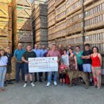 Un groupe de personnes tenant un grand chèque devant un fond de caisses de pomme de terre