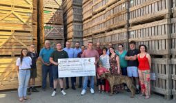 Un groupe de personnes tenant un grand chèque devant un fond de caisses de pomme de terre