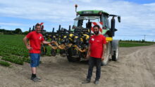 Deux producteurs de légumes debout devant un tracteur dans un champ de production