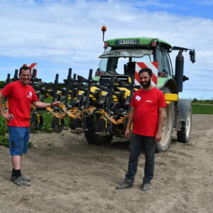 Deux producteurs de légumes debout devant un tracteur dans un champ de production