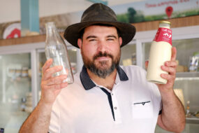 Un homme souriant avec un chapeau de cow-boy avec dans les mains deux bouteilles, une vide et une remplie de lait