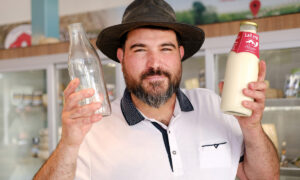 Un homme souriant avec un chapeau de cow-boy avec dans les mains deux bouteilles, une vide et une remplie de lait