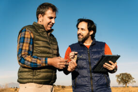 Deux hommes discutent dans un champ, l'un d'entre eux tient une tablette numérique