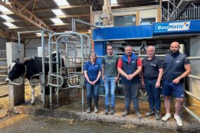 Quatre éleveurs et une éleveuse devant la stalle d'un robot de traite d'où sort une vache de race Holstein