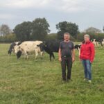 Un homme et une femme dans une prairie où pâturent des vaches laitières de race Prim'Holstein
