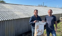 Deux hommes présentent un sac devant un bâtiment d'élevage à la toiture blanchie