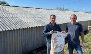 Deux hommes présentent un sac devant un bâtiment d'élevage à la toiture blanchie