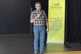 Une personne sur scène avec un micro devant un kakemono Eureden