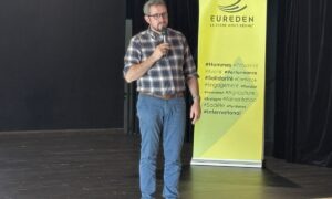 Une personne sur scène avec un micro devant un kakemono Eureden