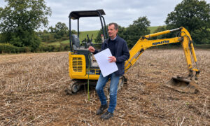 Un agronome, à côté d'une mini pelle, dans un champ sec après la récolte de colza