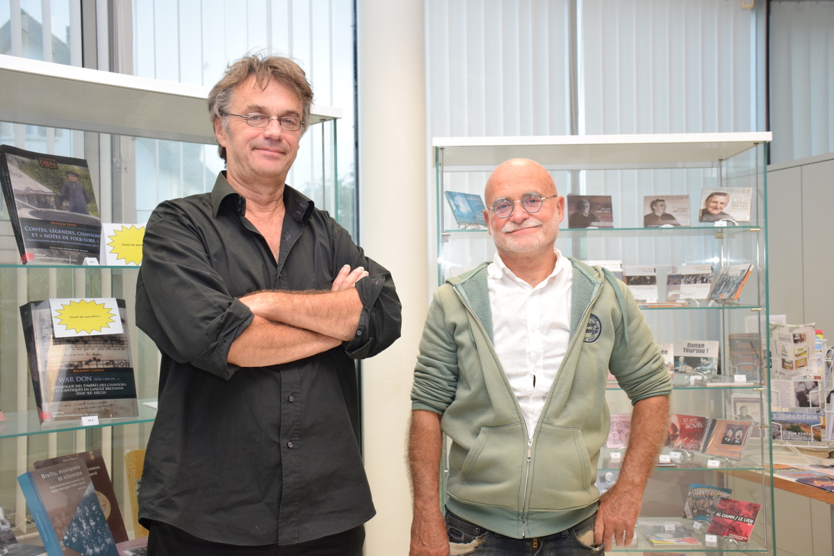 Deux personnes se tenant debout devant une vitrine d'ouvrages et de CD édités par l'association Dastum - Illustration Passeurs de mémoire 